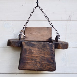 Puede incluir: Una caja de madera rústica con una tapa con bisagras cuelga de una cadena de metal. La caja está desgastada y tiene un acabado marrón oscuro.