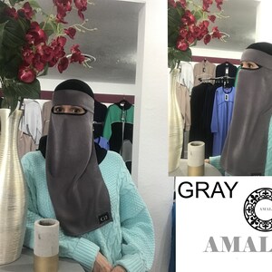 May include: Gray niqab with a black headband and eye opening. The niqab is made of a soft, stretchy fabric. The niqab is displayed on a mannequin in a store.