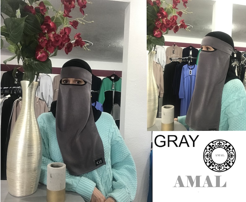 May include: Gray niqab with a black headband and eye opening. The niqab is made of a soft, stretchy fabric. The niqab is displayed on a mannequin in a store.