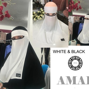 May include: White niqab with a black under-scarf. The niqab has a white face covering and a black band around the forehead. The text "GI" is visible on the niqab. The text "WHITE & BLACK" and "AMAL" are visible in the image.