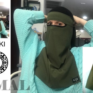 May include: A khaki green niqab with a black band around the forehead and a black eye mask. The niqab has a small black label with the text "G.II" on the bottom right corner.