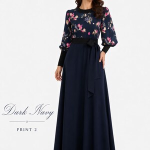 Puede incluir: Un vestido largo hasta el suelo en azul marino oscuro con estampado floral en el corpi&ntilde;o y mangas largas. La prenda incluye una falda azul marino lisa, cuello redondo negro, pu&ntilde;os negros y un cintur&oacute;n de tela a juego en la cintura. El texto dice Dark Navy PRINT 2.