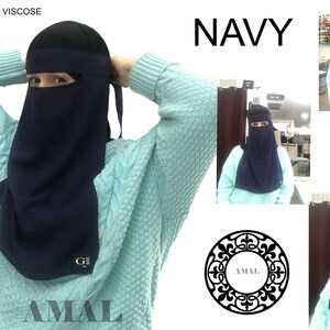 May include: A navy blue niqab with a face opening and a long, flowing back panel. The niqab is made of polyester and viscose and has the word "AMAL" printed on the bottom. The image also shows the niqab being worn by a person.