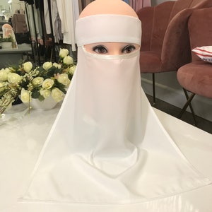 May include: White niqab with a white headband. The niqab is made of a soft, flowing fabric and has a wide, flowing design.