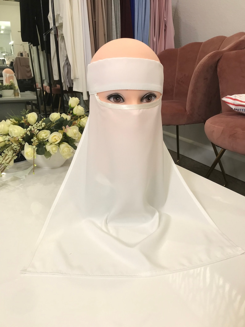 May include: White niqab with a white headband. The niqab is made of a soft, flowing fabric and has a wide, flowing design.