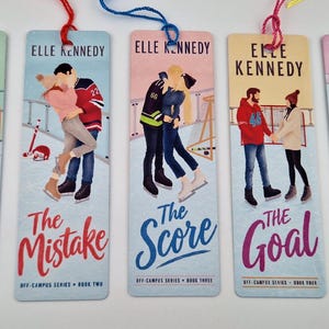 Peut inclure: Cinq marque-pages rectangulaires en papier illustrant la série Off-Campus d'Elle Kennedy. Chaque marque-page présente une scène unique avec des personnages, les titres The Deal, The Mistake, The Score, The Goal et The Legacy, ainsi que des pompons colorés.