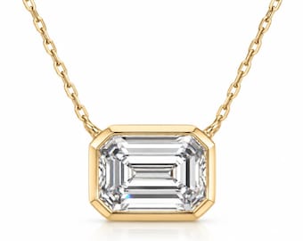 May include: A gold necklace featuring a rectangular emerald-cut clear gemstone set in a polished gold bezel setting. The pendant is suspended from a delicate gold chain with small, uniform oval links that connect to the top of the metal frame.