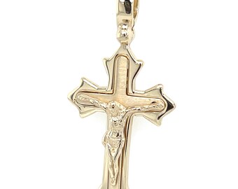May include: Gold-toned pendant necklace featuring a detailed crucifix with the figure of Jesus Christ. The cross has ornate edges and is suspended from a delicate chain. The pendant is likely made of gold or a gold-colored metal.