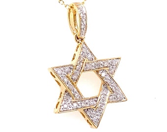 Puede incluir: Un colgante de estrella de David en oro con un diseño de seis puntas. La superficie de la estrella está incrustada con numerosas piedras pequeñas, claras y brillantes. El colgante está unido a una fina cadena de oro mediante una reasa dorada.