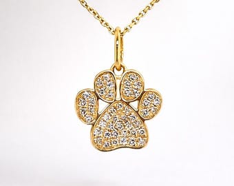 May include: A gold-toned necklace featuring a pendant shaped like a paw print. The pendant is encrusted with numerous small, clear, sparkling stones that cover the entire surface of the paw pad and the four individual toes of the design.
