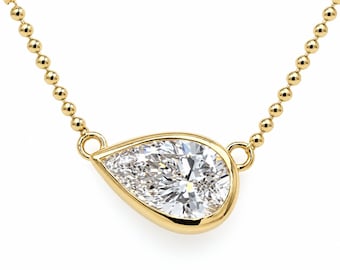 May include: A gold necklace featuring a pear-shaped clear gemstone set in a smooth gold bezel. The pendant is attached to a delicate gold ball chain that extends from both sides of the setting, creating a refined and polished jewelry piece.