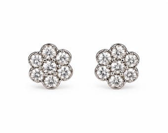 May include: A pair of stud earrings crafted from silver-toned metal, each featuring a cluster of seven round, clear, faceted stones arranged in a floral pattern. The stones are set closely together, creating a circular, flower-like shape.