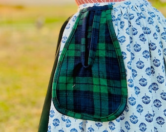 May include: A historical-style outfit featuring a red and white striped corset, a white blouse, and a blue and white patterned skirt. A green and black plaid pocket is attached to the skirt. The outfit is designed for historical reenactment or costume events.