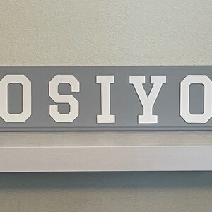 May include: A gray wooden sign with the name "OSIYO" written in white block letters.