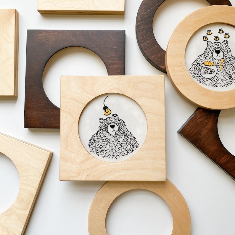 Puede incluir: Un conjunto de seis aros de bordado de madera con una variedad de dise&ntilde;os. Los aros son todos cuadrados y tienen un acabado de madera clara. Los dise&ntilde;os incluyen un oso con una bombilla, un oso con miel y un oso con una flor.