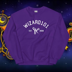 Peut inclure: Un sweat-shirt ras du cou violet avec le texte blanc "WIZARD101" en arc. En dessous, le texte "EST. W 2008" en blanc. Le sweat-shirt est fait d'une matière douce.
