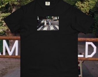 Puede incluir: Camiseta negra con un estampado gráfico blanco de dos personas caminando por un paso de cebra. El gráfico es una recreación de la famosa portada del álbum de los Beatles.