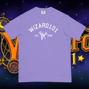 May include: A light purple t-shirt with the text "WIZARD101" in white, arched across the top. Below the text is a stylized "W" logo and the text "EST. 2008". The shirt is a crew neck style.