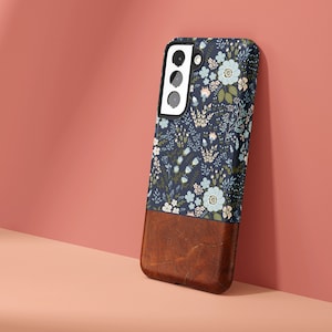 May include: A blue and white floral phone case with a brown leather bottom. The case has a cutout for the camera lens.
