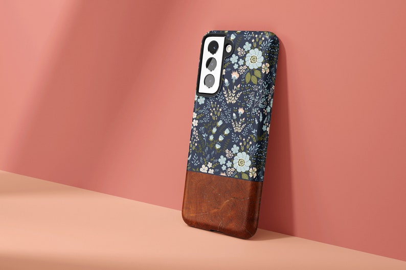 May include: A blue and white floral phone case with a brown leather bottom. The case has a cutout for the camera lens.