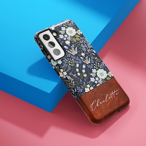 May include: A blue and white floral phone case with a brown leather bottom. The leather bottom has the name "Charlotte" written in white script.