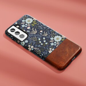 May include: A navy blue phone case with a floral pattern and a brown wood-like accent. The case has a cutout for a triple camera lens.