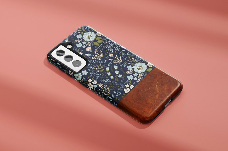 May include: A navy blue phone case with a floral pattern and a brown wood-like accent. The case has a cutout for a triple camera lens.