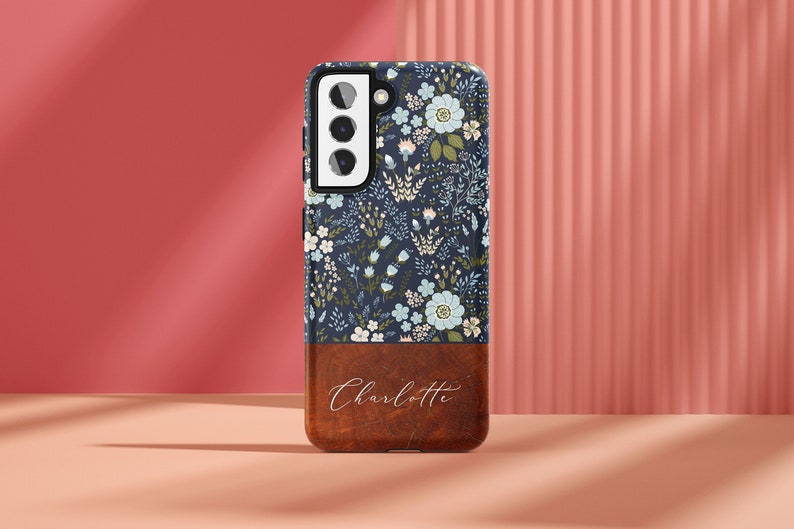 May include: A blue and white floral phone case with a brown wood-look bottom and the name "Charlotte" engraved on it.