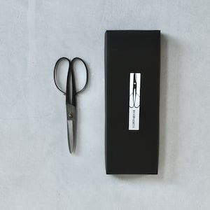 Puede incluir: Un par de tijeras negras con mango plateado en una caja negra con una etiqueta blanca que dice "Tijeras japonesas".