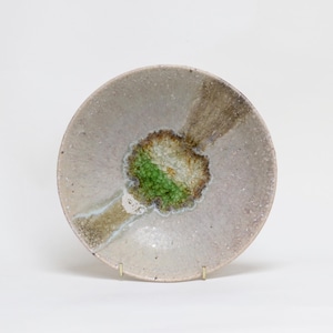 Puede incluir: Un plato de cerámica hecho a mano con un diseño único. El plato presenta un fondo gris claro con un área central de tonos verdes y marrones. El plato es redondo y tiene una superficie ligeramente texturizada, mostrando la artesanía.