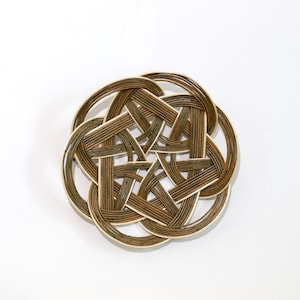 May include: A handcrafted, circular decorative basket with an intricate woven design. The basket features a star-like pattern in shades of brown and beige, with a natural, organic aesthetic. The basket is made of thin, woven strips.