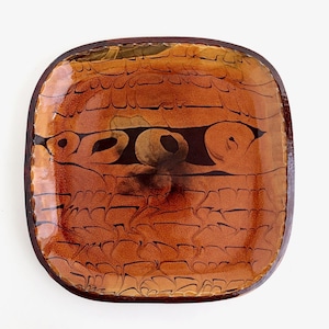 May include: A square glass dish with rounded corners, featuring a glossy finish in shades of amber and brown. The surface displays a distinct crackled texture with dark brown horizontal lines and abstract swirling patterns throughout the center.