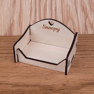 May include: A small wooden box with a heart cutout and the word "Snoopy" engraved on the top. The box is made of light wood and has a dark brown stain.