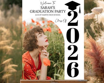 May include: A graduation party sign on an easel. The sign reads "Welcome to Sarah's Graduation Party, August Martin High School, Class of 2026." A photo of a woman in a red dress is on the sign. The numbers "2026" are vertically displayed.
