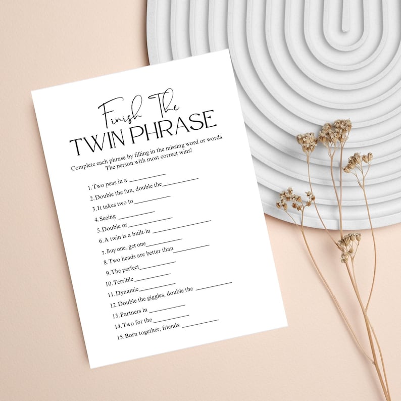 May include: A white paper game sheet titled "Finish The Twin Phrase". The game challenges players to complete phrases. The sheet is on a neutral background with decorative elements, suitable for a bridal shower or baby shower activity.