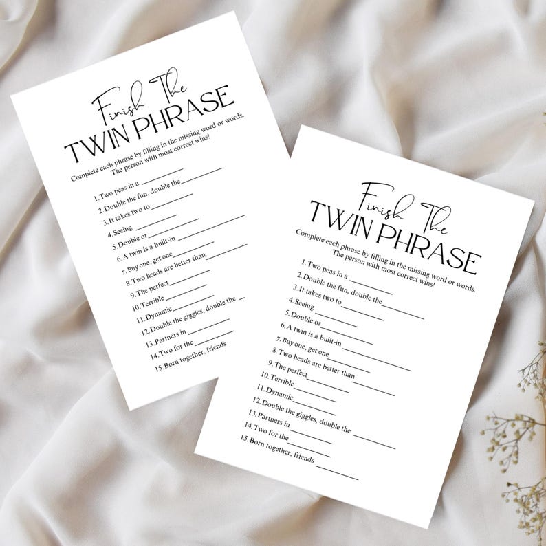 May include: Two white paper sheets with the text "Finish The Twin Phrase" in elegant script. The sheets contain fill-in-the-blank questions, designed as a game. The text is in black, and the background is a soft, neutral color.