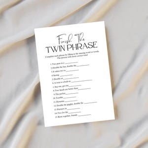 May include: A white card with the text "Finish The Twin Phrase" in a script font. The card has fill-in-the-blank phrases such as "Two peas in a" and "Double the fun, double the". The card is designed for a game.