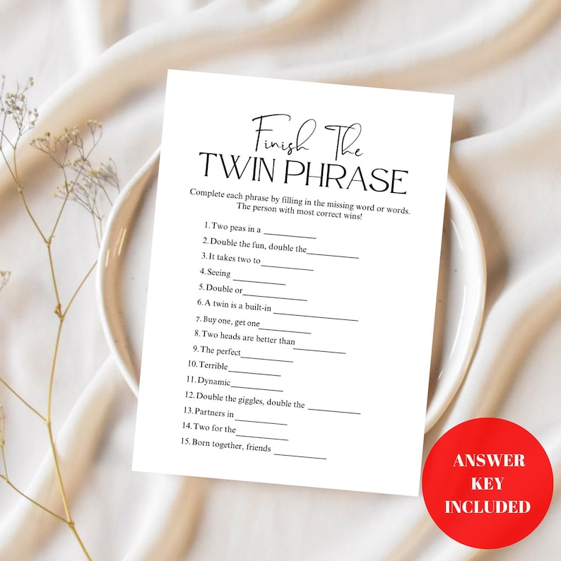 May include: A white card with the text "Finish The TWIN PHRASE" printed in black, with fill-in-the-blank phrases. A red circle with "ANSWER KEY INCLUDED" is in the lower right corner. The card is on a white plate.