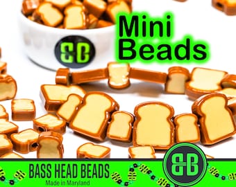 Puede incluir: Un bol lleno de pequeñas cuentas de pan de color marrón y beige. Las cuentas están esparcidas alrededor del bol y sobre una superficie blanca. El texto "Mini Beads" está escrito en letras verdes sobre un fondo blanco. El texto "Bass Head Beads Made in Maryland" está escrito en letras negras sobre un fondo verde. El logotipo "BB" está en letras verdes sobre un fondo blanco.