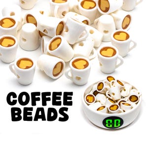 Puede incluir: Un gran grupo de cuentas de cerámica blanca en forma de taza de café con un diseño de corazón marrón. Las cuentas están esparcidas sobre una superficie blanca. El texto "COFFEE BEADS" está impreso en negro debajo de las cuentas. Un pequeño tazón blanco lleno de las mismas cuentas se muestra en la esquina inferior derecha de la imagen.