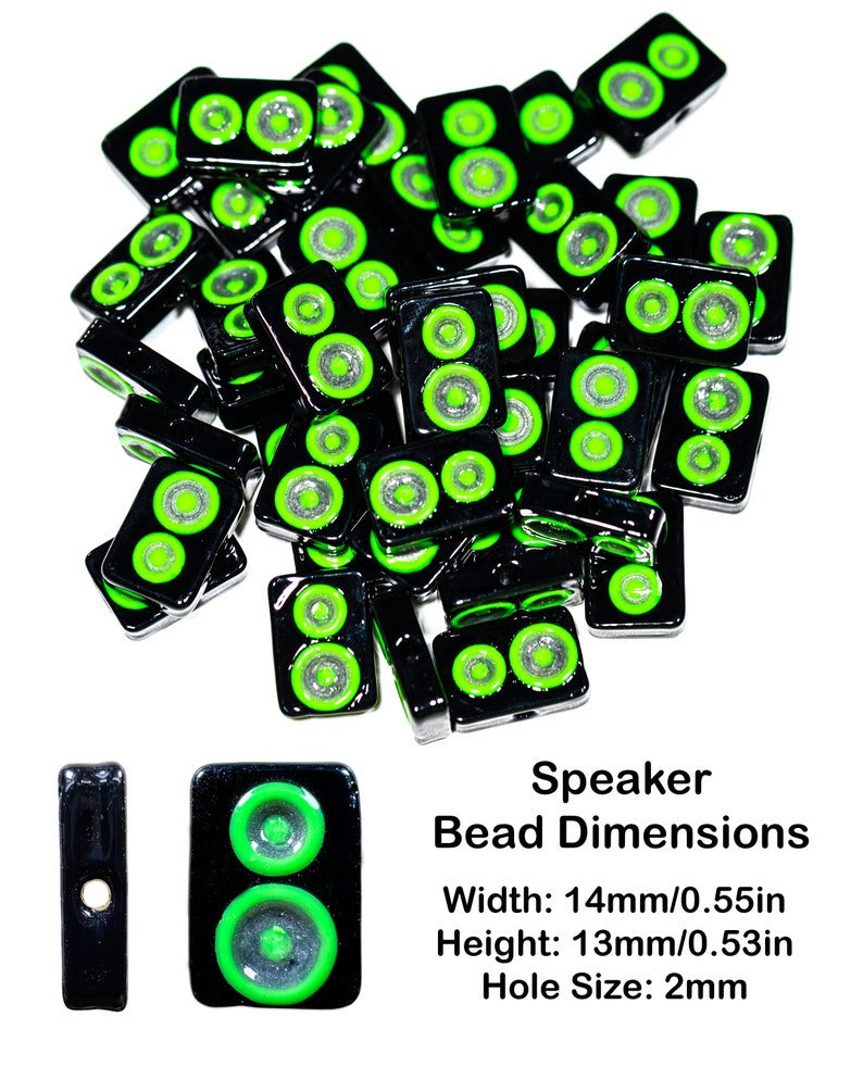 May include: A pile of black and green speaker-shaped glass beads. Each bead has two green circles with a silver center. The beads are 14mm wide and 13mm high with a 2mm hole.