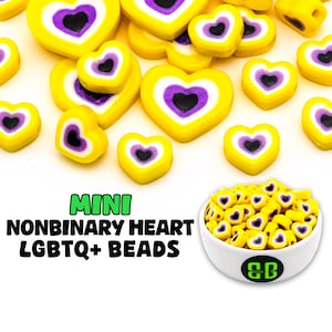 May include: Yellow heart-shaped beads with white and purple accents, scattered across a white surface. The beads are in a small white bowl with the text "MINI NONBINARY HEART LGBTQ+ BEADS". The bowl has a green and black logo.