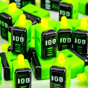 May include: Bright green and black rectangular objects with a yellow top and the number "100" in white. The objects are scattered across a white surface. The objects have a digital display.