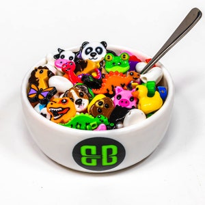 May include: A white bowl filled with colorful plastic animal figurines. The bowl has a green and black logo that says "BB".
