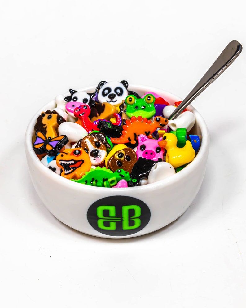 May include: A white bowl filled with colorful plastic animal figurines. The bowl has a green and black logo that says "BB".