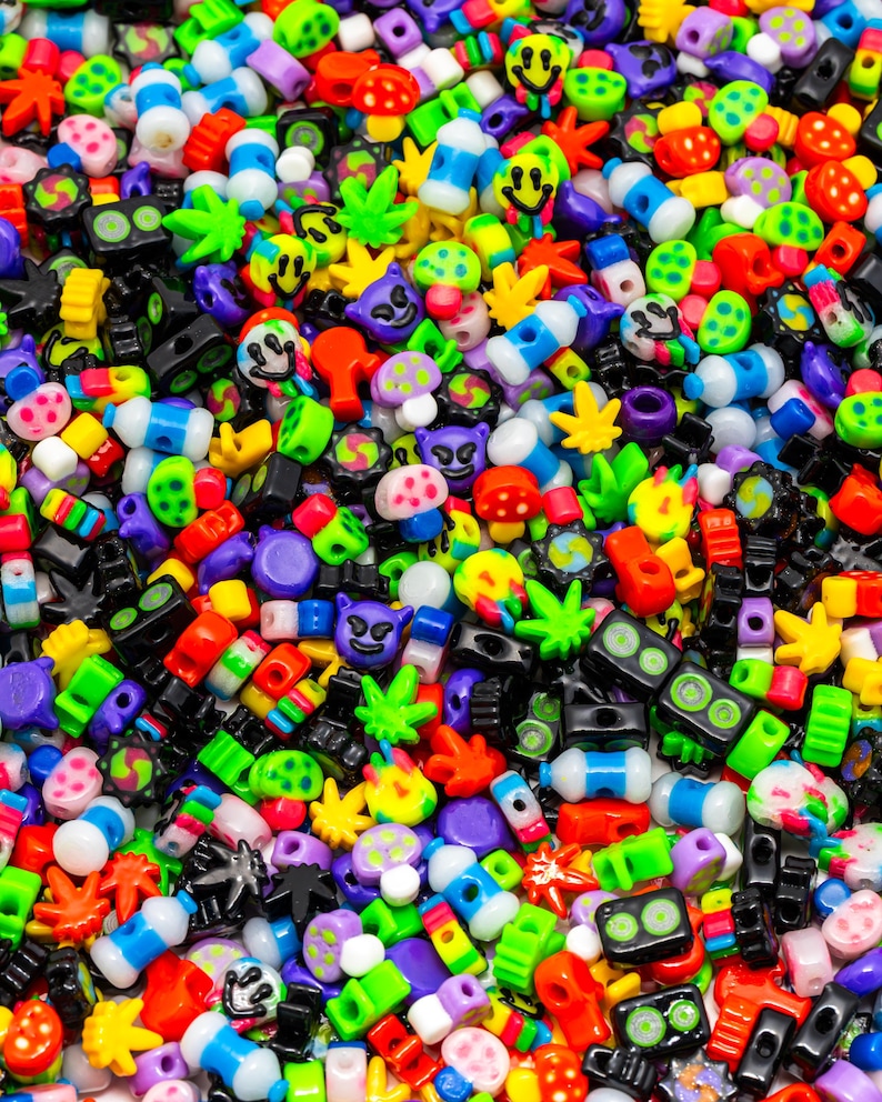 May include: A vibrant assortment of colorful plastic beads in various shapes. The beads include smiley faces, mushrooms, marijuana leaves, and other novelty designs. The color palette is diverse, featuring red, green, blue, yellow, and purple.