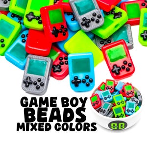 May include: A bowl filled with colorful Game Boy beads in various colors, including red, blue, green, and gray. The beads are shaped like miniature Game Boy handheld consoles. The text "GAME BOY BEADS MIXED COLORS" is printed below the bowl.