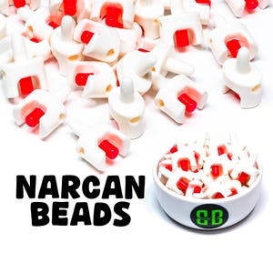 Puede incluir: Un bol lleno de cuentas Narcan blancas y rojas. Las cuentas son pequeñas y redondas, con un punto rojo en cada una. El bol es blanco con un logotipo verde que dice "SB". El texto "Narcan Beads" está escrito en letras negras sobre un fondo blanco.