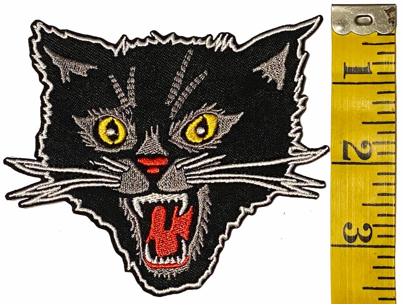 May include: Black and white embroidered patch of a snarling black cat's head with yellow eyes and red mouth. The patch is approximately 5 cm wide.