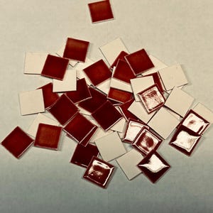 May include: A collection of small, square tiles. The tiles have a glossy, deep red surface on one side and a white surface on the other. The tiles are scattered across a light-colored surface, creating a mosaic effect.